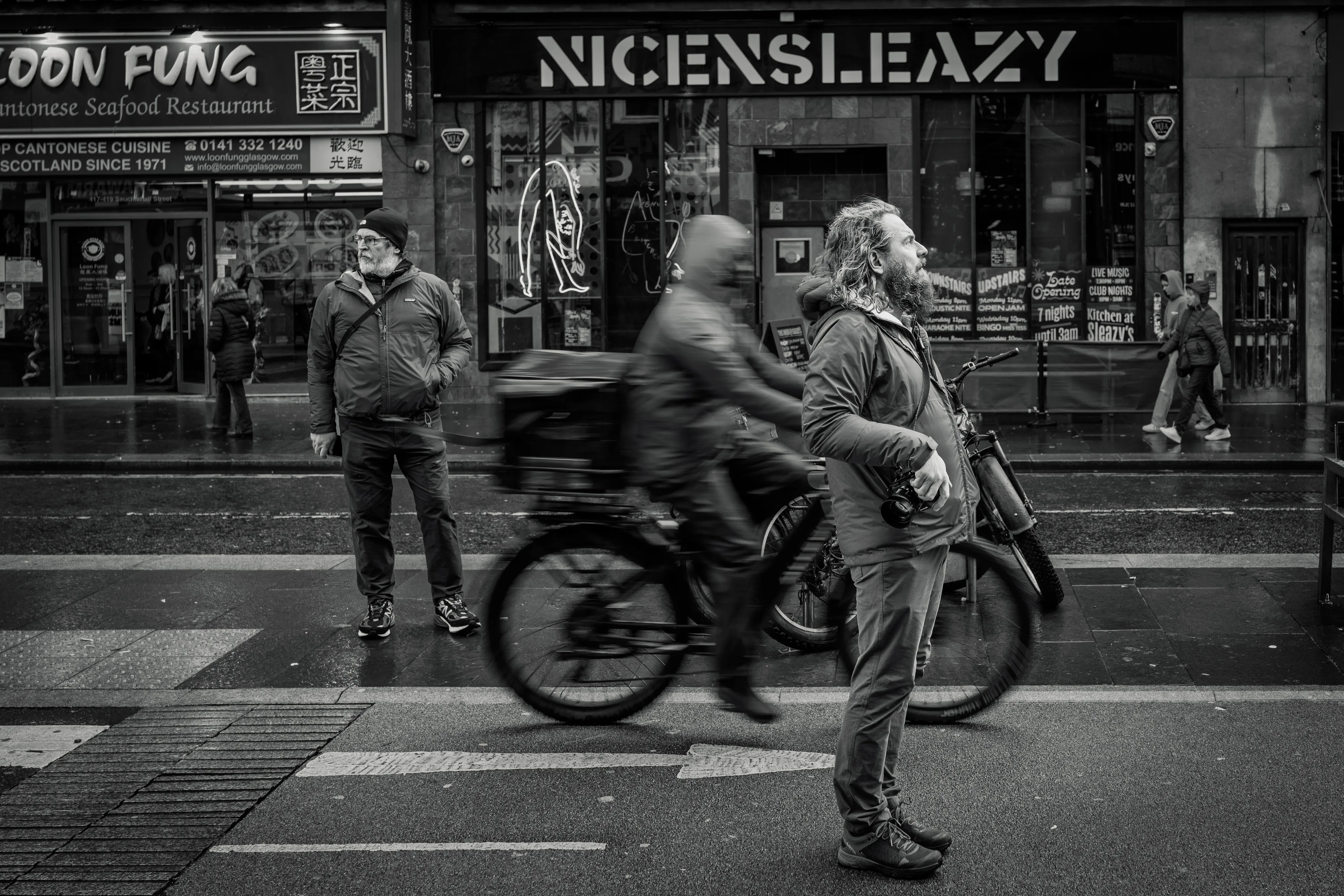 Rick Lepage and Hudson Henry photographing on Sauchiehall Street as a delivery rider passes between them.
